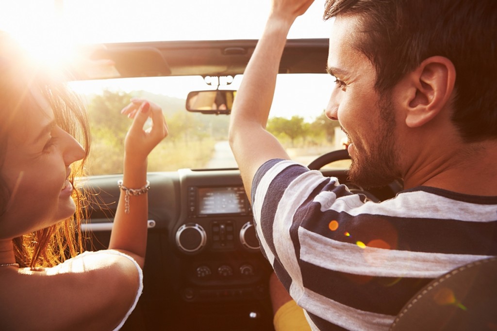 Young Couple Driving Along Country Road In Open Top Car