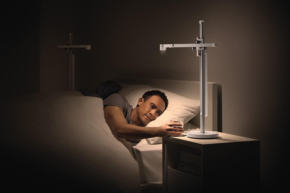 Lightcycle being used by a couple in bed, man reaching for glass of water, light is personal/targeted on him, warm low lux light, 2700K