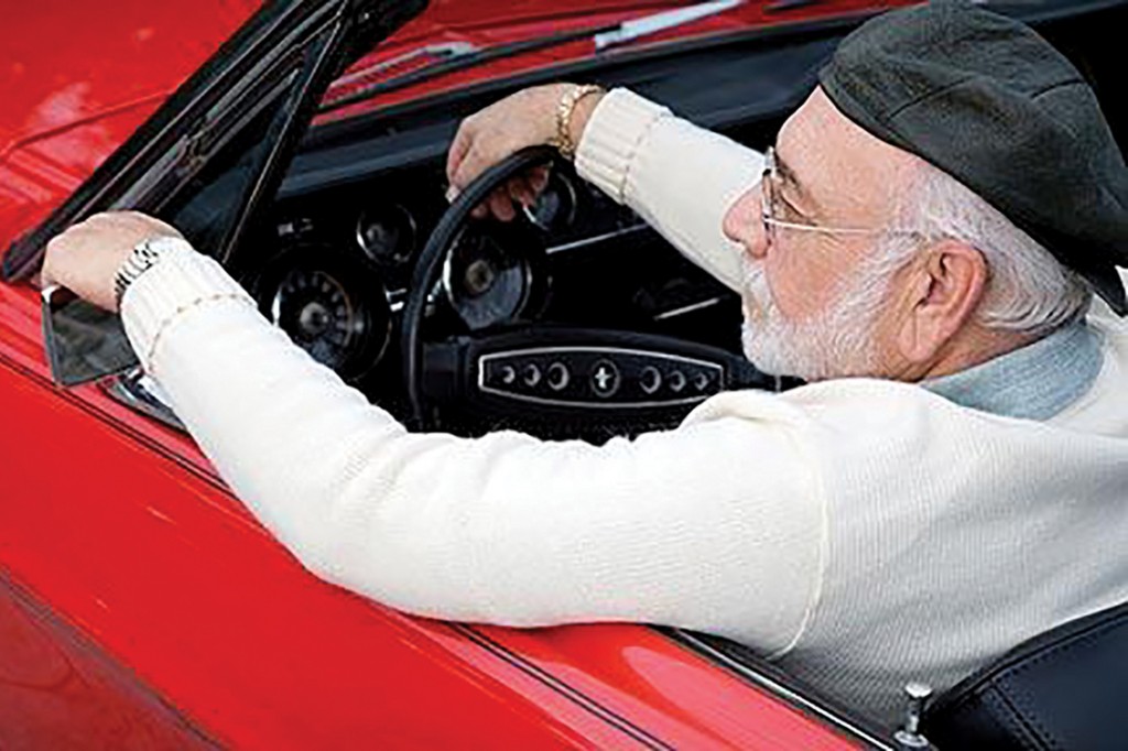 A7TMWG A senior man in a sports car adjusting his wing mirror